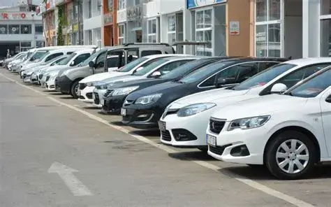 صف طويل من سيارات سيدان بيضاء وداكنة مصطفة على جانب شارع أمام متاجر