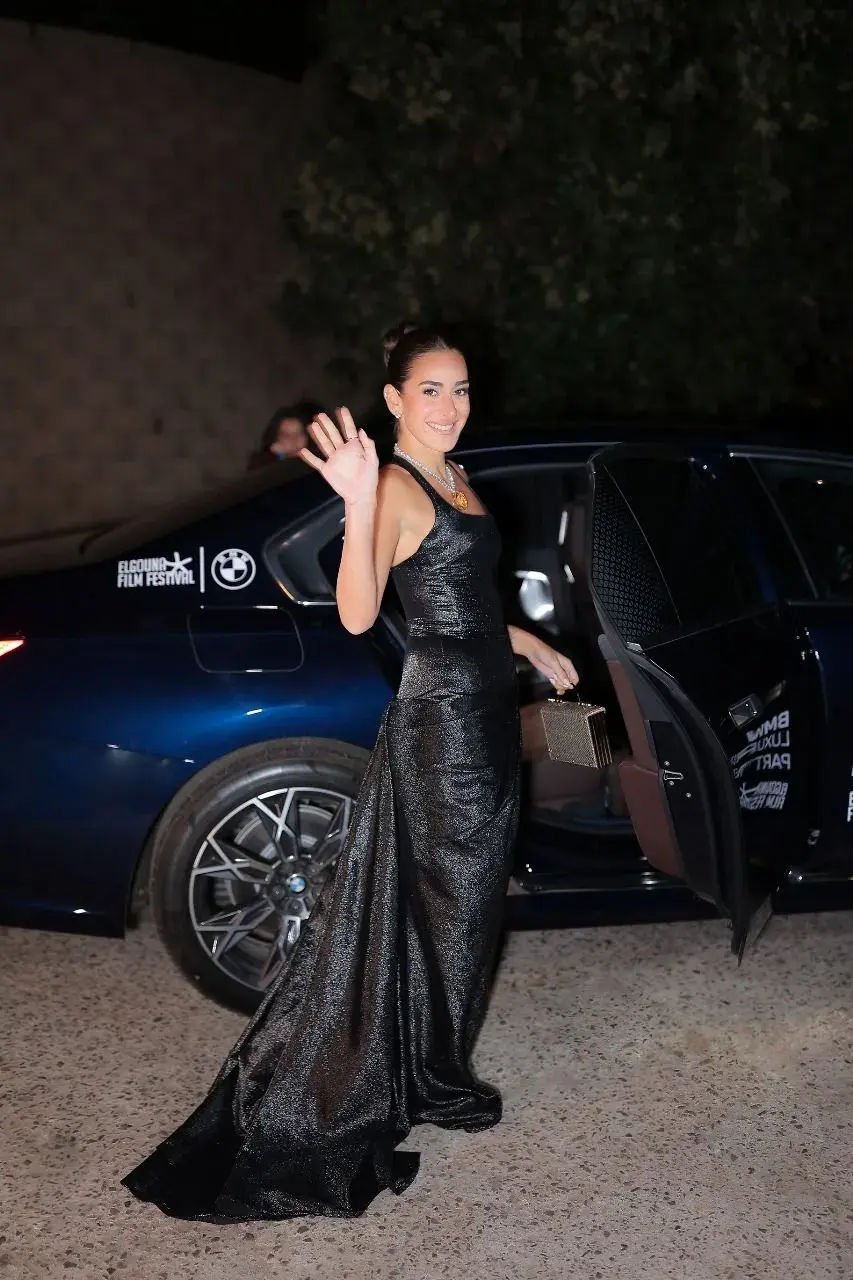 ضيفة بفستان أسود تحيي الجمهور لدى نزولها من سيارة BMW بالمهرجان