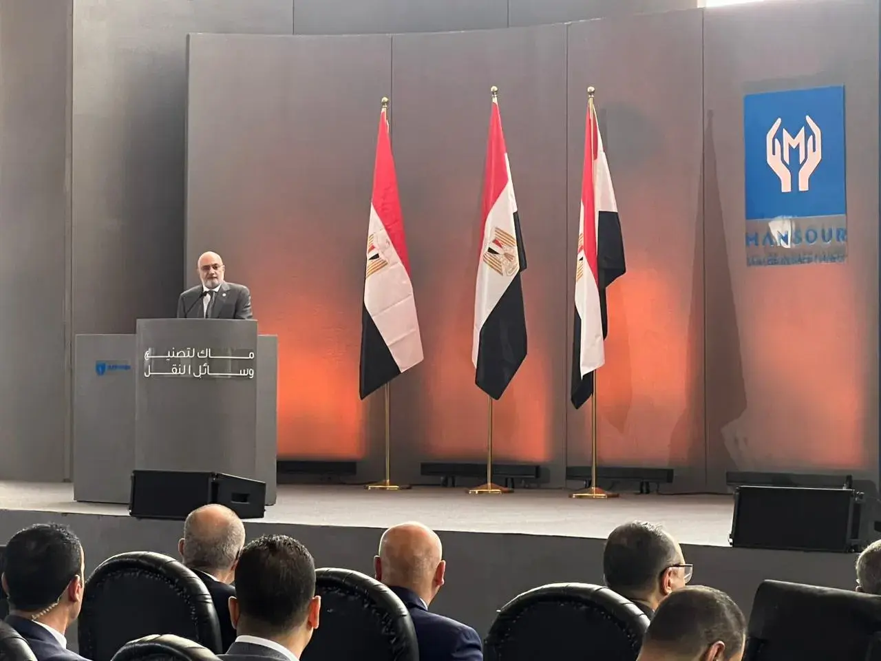 متحدث على المنصة خلال مؤتمر تدشين مصنع ماك وخلفه أعلام مصر