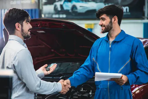 فني صيانة يصافح عميلًا أمام سيارة مفتوحة الغطاء داخل مركز خدمة