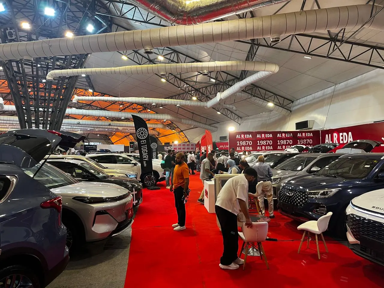 زوار بين سيارات SUV معروضة على سجادة حمراء داخل قاعة معرض Auto Center Point